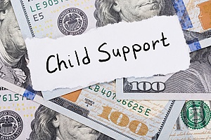 child support written on a white piece of paper on top of hundred dollar bills