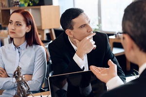 divorcing couple looks in different directions listening to lawyer who sitting at table