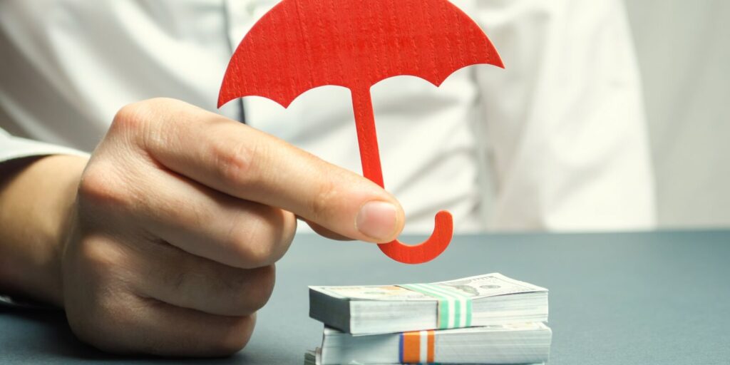 insurance agent holds a red umbrella over dollar bills
