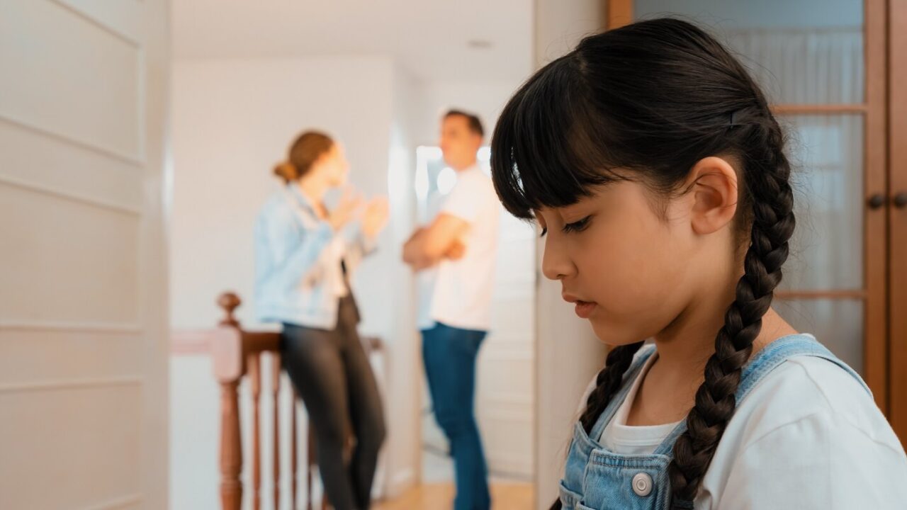 unhappy young girl huddle in corner crying and sad while her parent arguing in background