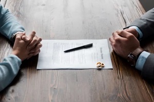 cropped shot of divorce lawyer and client sitting at table with divorce decree and wedding rings