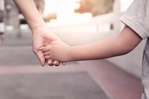 parent holds the hand of a small boy in the sunset