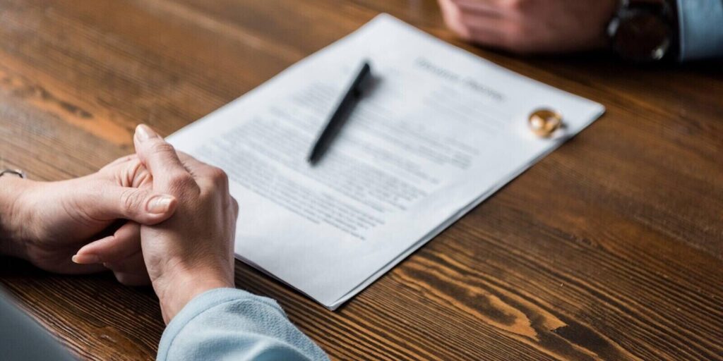 partial view of lawyer and client sitting at table with divorce decree and wedding rings