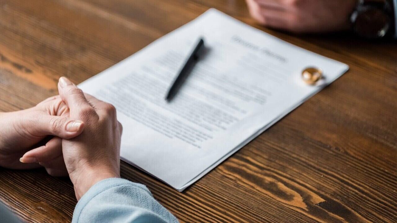 partial view of lawyer and client sitting at table with divorce decree and wedding rings