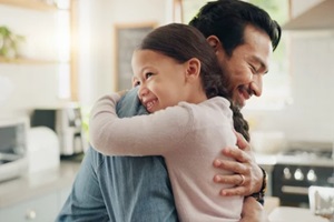 father and daughter hug in the kitchen for love, trust or bonding together in their home