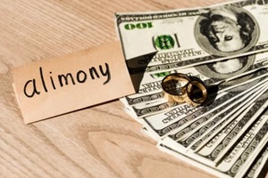 paper with alimony lettering near dollar banknotes and engagement rings