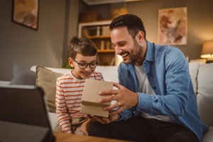 father and son open birthday present home with tablet on the table