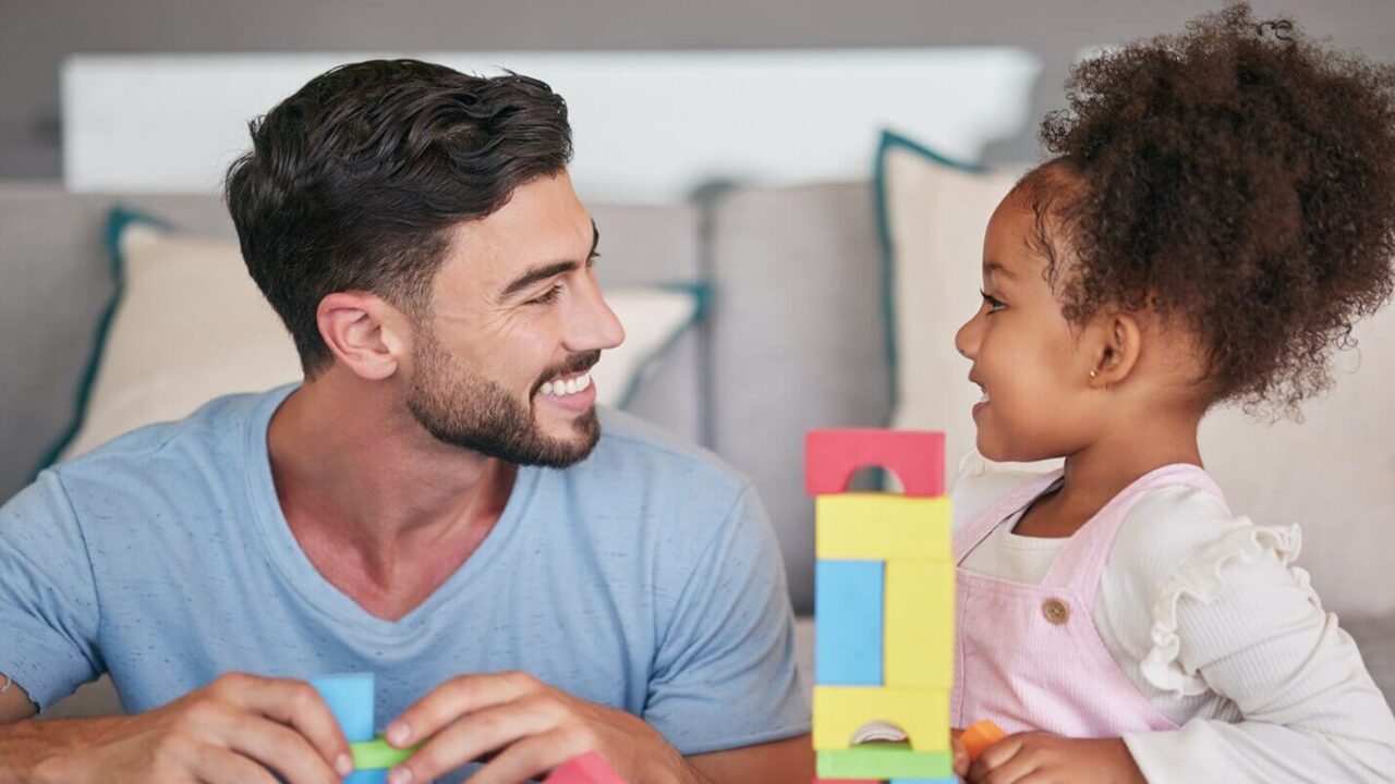 family and education with a girl and her father playing with building blocks in the living room of their home