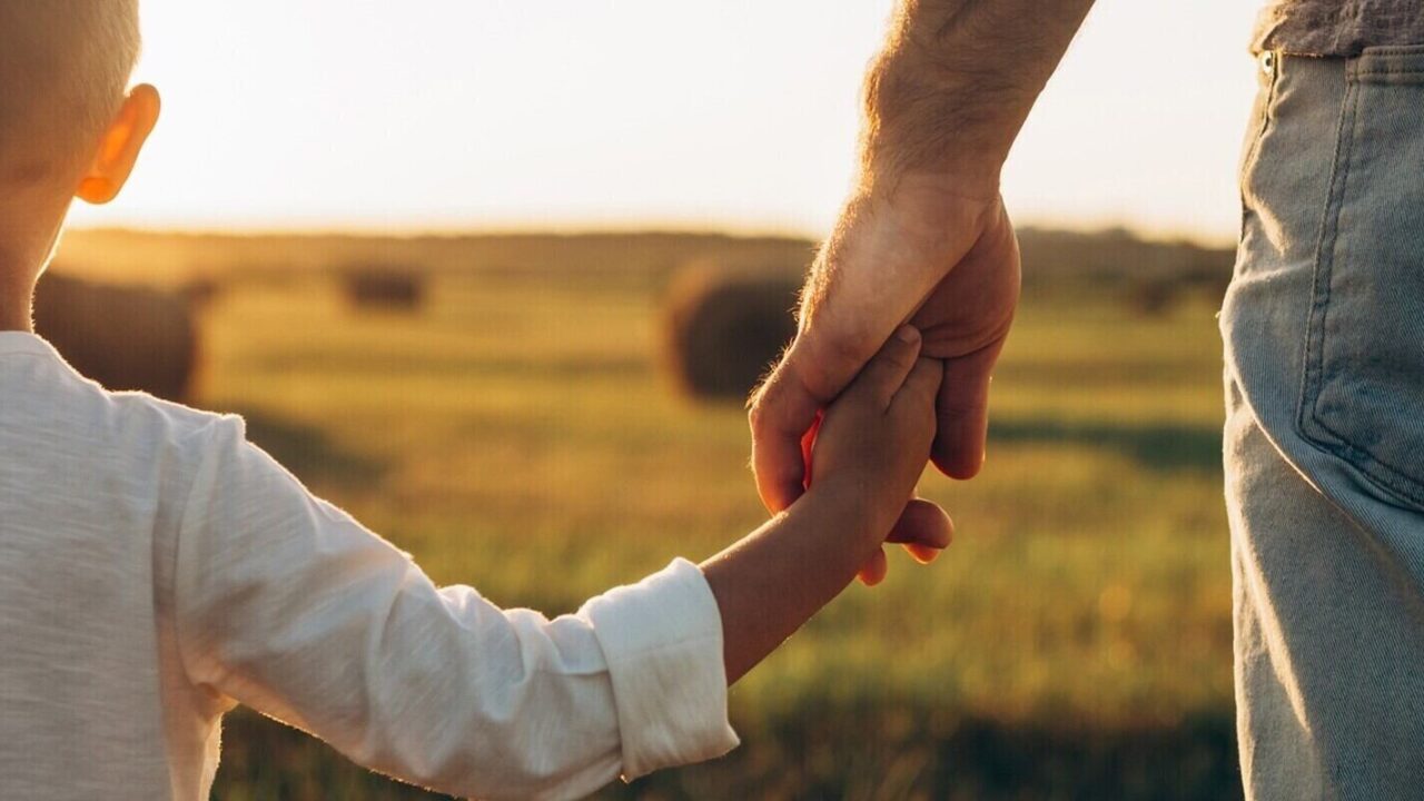 father's and his son holding hands at sunset field