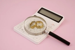 golden wedding rings under magnifying glass and calculator on pink background