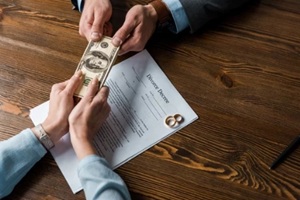partial top view of woman giving money to lawyer about divorce decree with wedding rings