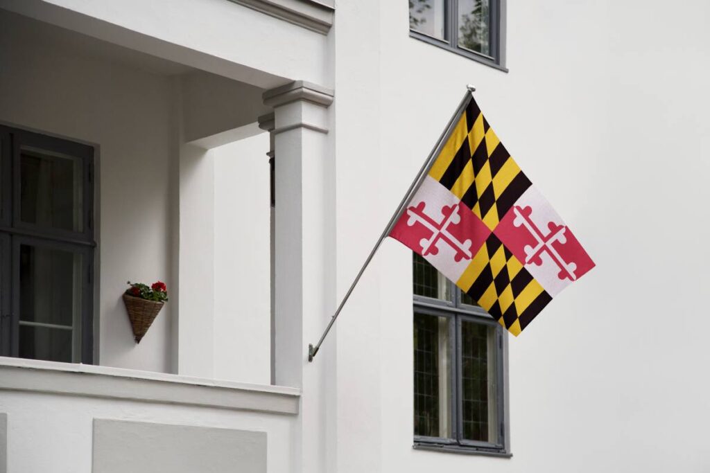 Maryland flag. Maryland state flag hanging on a pole in front of the house. State flag waving on a home displaying on a pole on a front door of a building.Flag raised at a full staff.