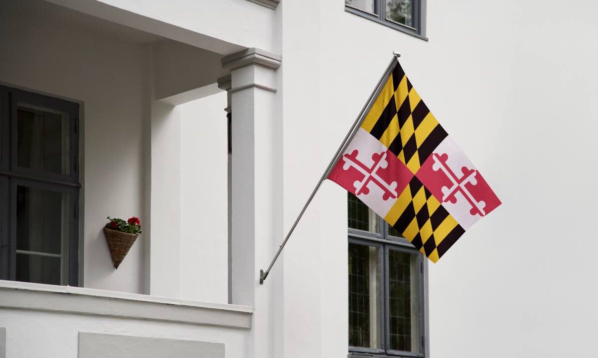 Maryland flag. Maryland state flag hanging on a pole in front of the house. State flag waving on a home displaying on a pole on a front door of a building.Flag raised at a full staff.