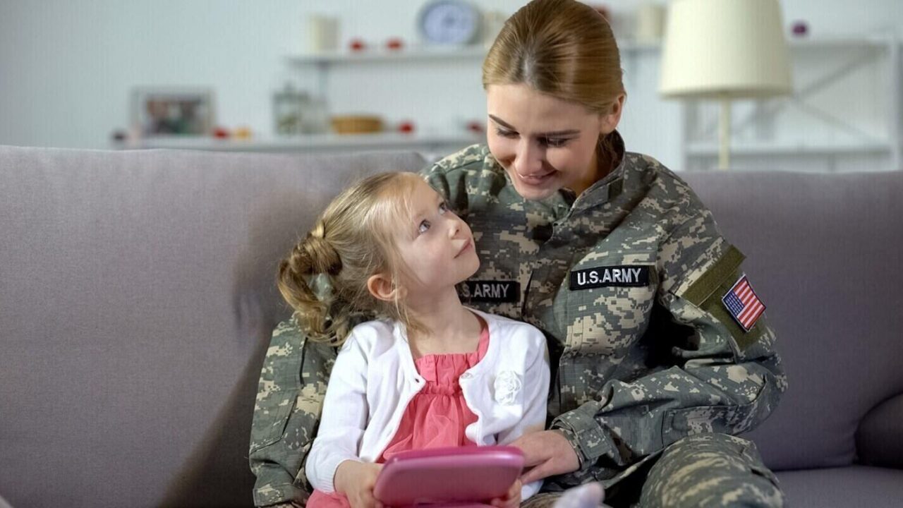 mother in US army uniform and little daughter playing game on tablet together