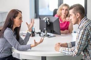 woman gesticulates to a man angry over disagreement with demale mediator sitting behind the table in the background