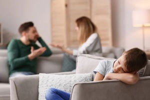 little unhappy boy sitting in armchair while parents arguing at home