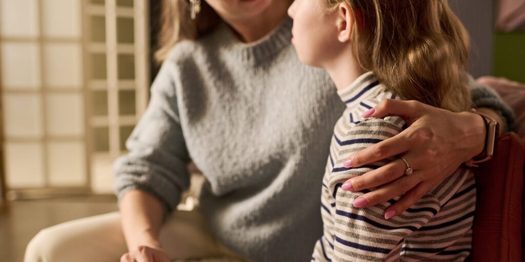 caucasian mother comforting teenage daughter while holding hands and embracing shoulder during serious home conversation