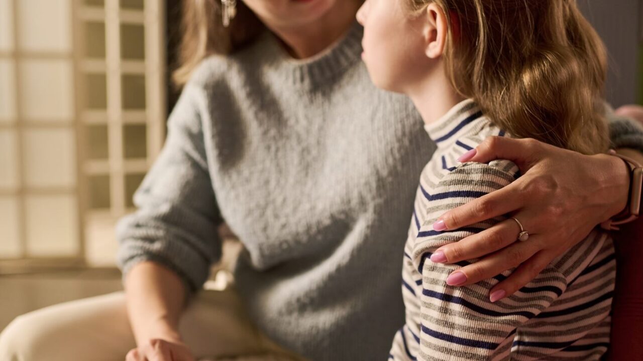 caucasian mother comforting teenage daughter while holding hands and embracing shoulder during serious home conversation