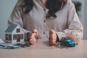 hands dividing assets between house model and toy car with piggy bank for financial budget allocation and asset planning